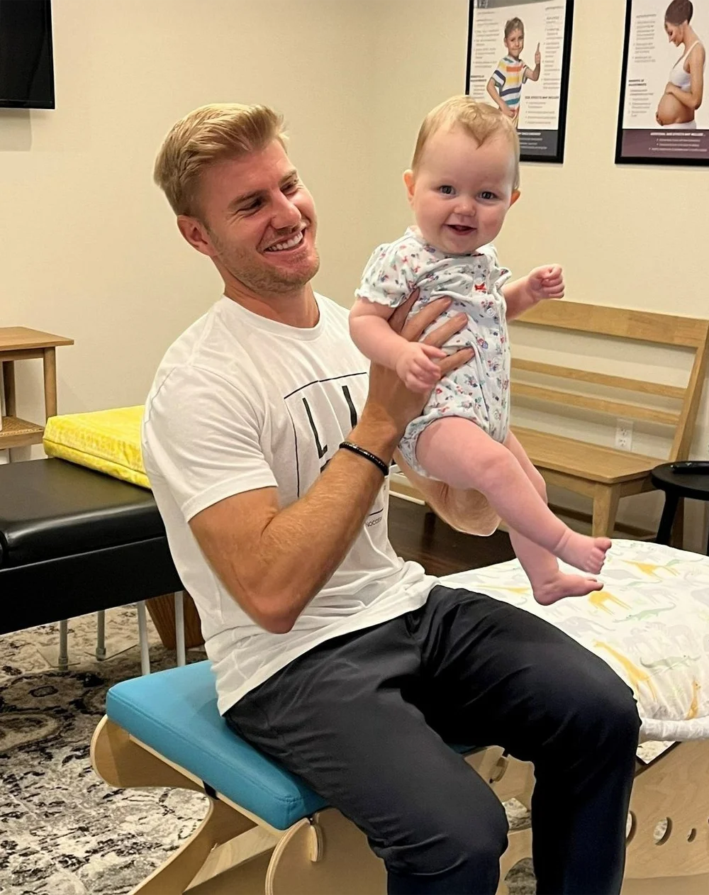 Dr. Brett Lukas lifting a smiling baby off of the adjustment table after successful treatment