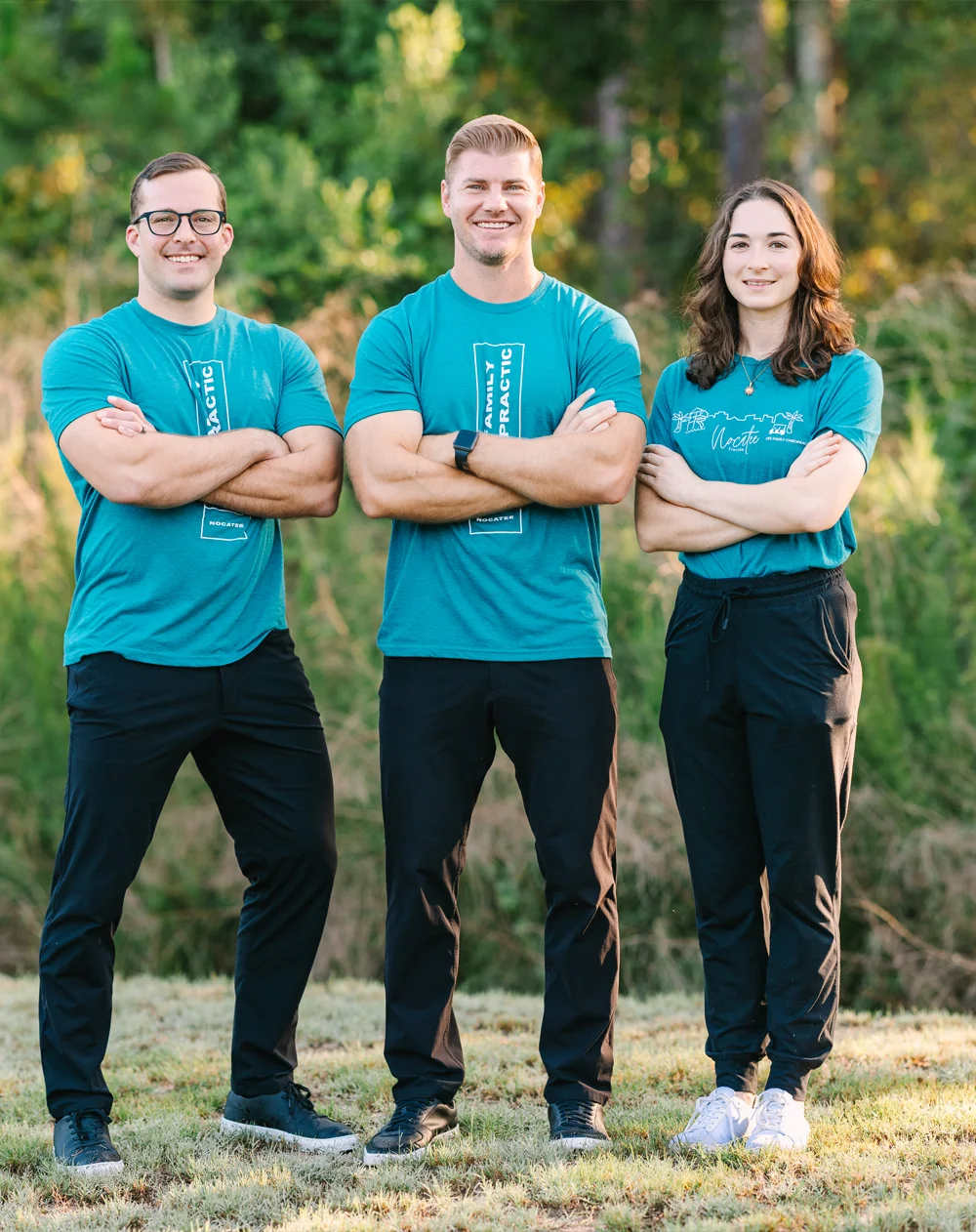 Chiropractor Ponte Vedra FL Brett Lukas With Team A group photo of 3 doctors standing close together in black pants and blue clinic shirts